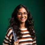 long brown hair in loose waves, wearing trendy glasses, a horizontal striped sweater